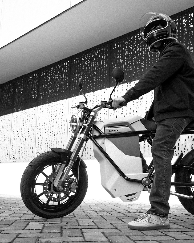 LAND DISTRICT rider in helmet, monochrome lifestyle shot against a perforated metal façade